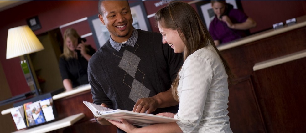 Two people standing in a hotel lobby looking at a binder.